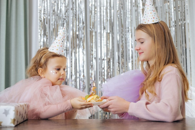 Belle ragazze con capelli biondi ricci e stelle sul viso in abiti rosa gonfi e cappellini da festa che si tengono insieme