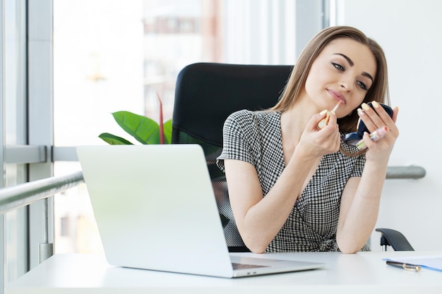 Pretty happy businesswoman doing make up in office