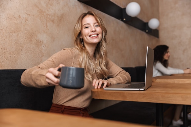 pretty happy girl sitting in cafe using laptop computer