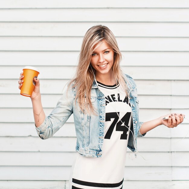 Photo pretty happy hipster girl enjoys music and drinks coffee