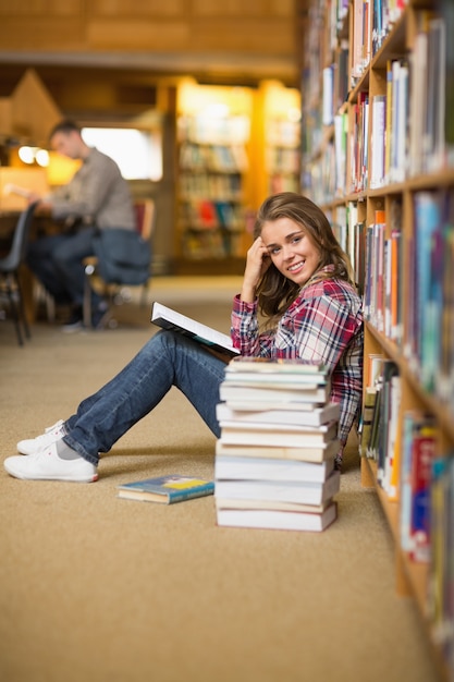 Pretty happy student reading book on library floor