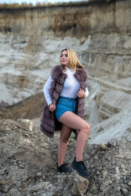 Pretty happy woman in fur coat on the sand rocks in nature