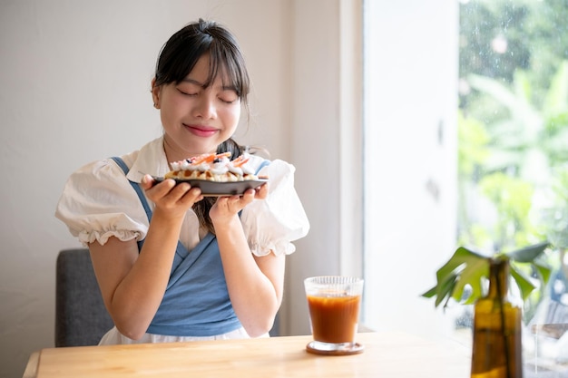 A pretty and happy young Asian woman smelling fresh baked croissant waffle at a coffee shop