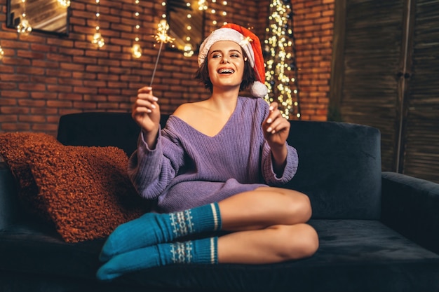 Pretty happy young brunette in christmas hat with sparkler in hands.