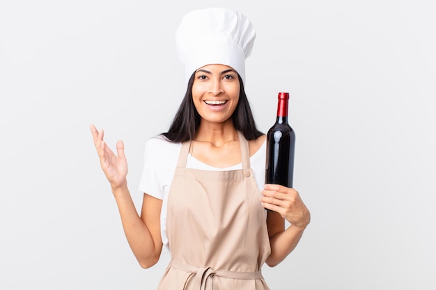 pretty hispanic chef woman feeling happy, surprised realizing a solution or idea and holding a bottle of wine