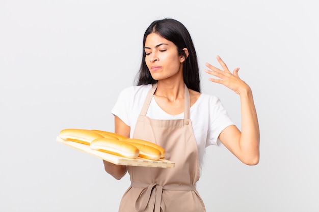 Pretty hispanic chef woman feeling stressed, anxious, tired and frustrated and holding a tray with bread buns