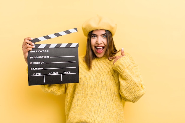 Pretty hispanic girl feeling happy and pointing to self with an excited cinema concept