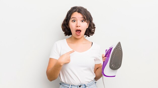 Pretty hispanic girl looking shocked and surprised with mouth wide open pointing to self laundry concept