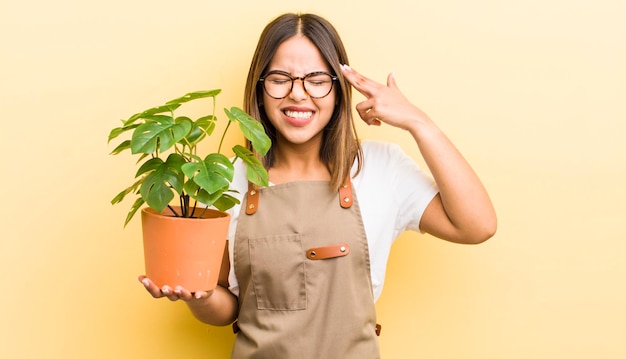 Pretty hispanic girl looking unhappy and stressed suicide gesture making gun sign plant concept