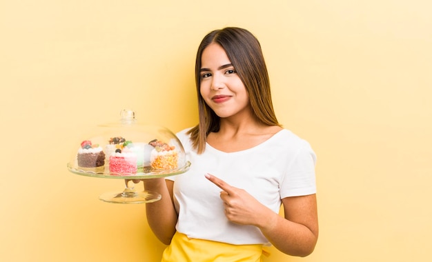 Pretty hispanic girl smiling cheerfully feeling happy and pointing to the side home made cakes concept