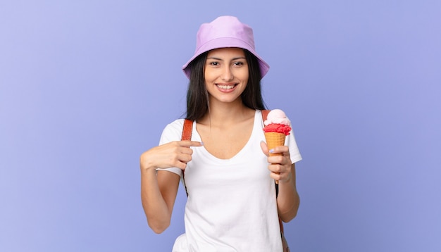 Pretty hispanic tourist feeling happy and pointing to self with an excited and holding an ice cream