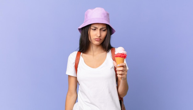 Pretty hispanic tourist feeling sad, upset or angry and looking to the side and holding an ice cream