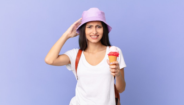 Pretty hispanic tourist feeling stressed, anxious or scared, with hands on head and holding an ice cream