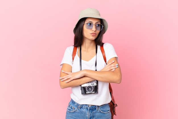 Pretty hispanic tourist shrugging, feeling confused and uncertain with a photo camera and a hat