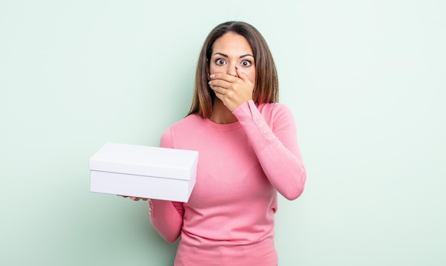 Pretty hispanic woman covering mouth with hands with a shocked. white box packaging concept