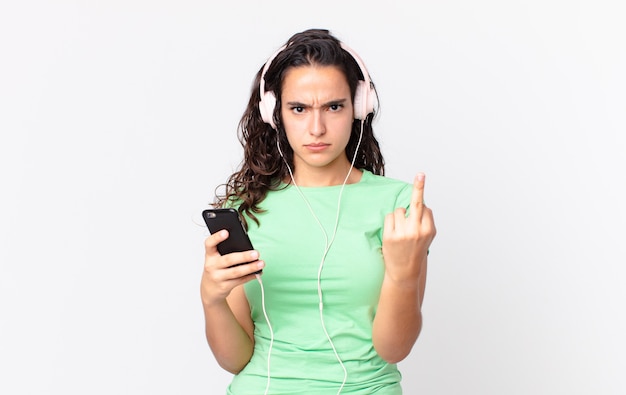 Довольно латиноамериканская женщина чувствует себя сердитой, раздраженной, мятежной и агрессивной с наушниками и смартфоном