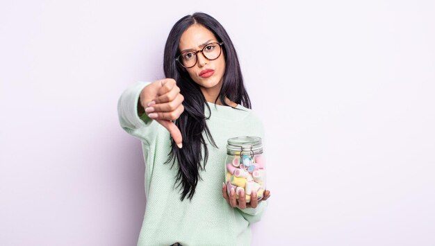 Pretty hispanic woman feeling cross,showing thumbs down jelly candies concept