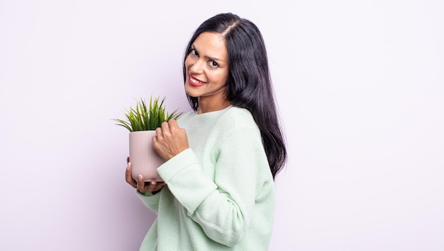 Pretty hispanic woman feeling happy and facing a challenge or celebrating. house plant concept