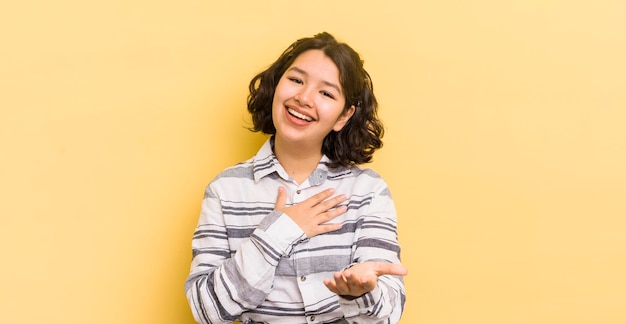 Pretty hispanic woman feeling happy and in love smiling with one hand next to heart and the other stretched up front