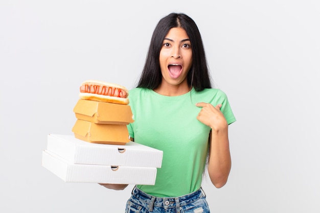Pretty hispanic woman feeling happy and pointing to self with an excited and holding take away fast food boxes