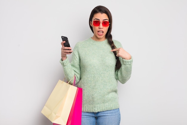 pretty hispanic woman feeling happy and pointing to self with an excited. shopping bags and costumer concept