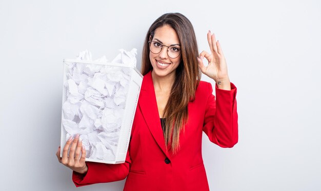 Pretty hispanic woman feeling happy, showing approval with okay gesture. paper balls failure concept