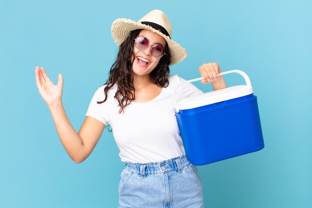 Pretty hispanic woman feeling happy, surprised realizing a solution or idea holding a portable refrigerator