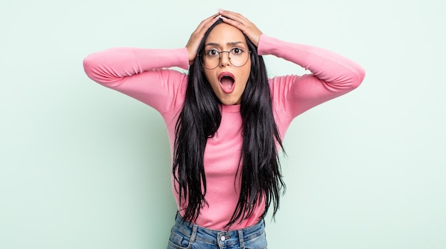 Pretty hispanic woman feeling horrified and shocked, raising hands to head and panicking at a mistake