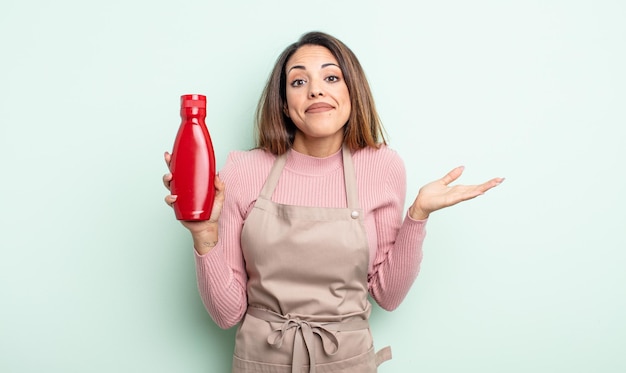 Pretty hispanic woman feeling puzzled and confused and doubting. ketchup concept