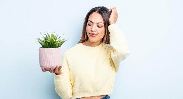 Pretty hispanic woman feeling puzzled and confused, scratching head. houseplant concept