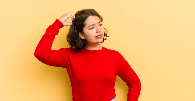 Pretty hispanic woman feeling puzzled and confused scratching head and looking to the side