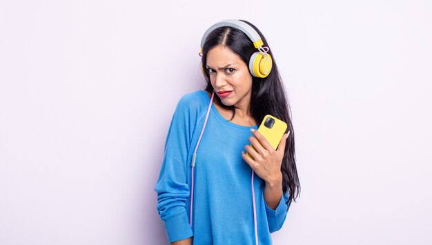 Pretty hispanic woman feeling puzzled and confused. smartphone and headphones concept