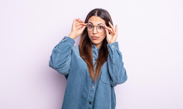 Pretty hispanic woman feeling shocked, amazed and surprised, holding glasses with astonished, disbelieving look