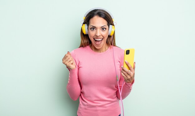 Pretty hispanic woman feeling shocked,laughing and celebrating success. smartphone and headphones concept