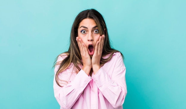 Pretty hispanic woman feeling shocked and scared looking terrified with open mouth and hands on cheeks