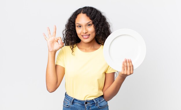 Pretty hispanic woman holding an empty clean dish