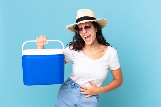Pretty hispanic woman laughing out loud at some hilarious joke holding a portable refrigerator
