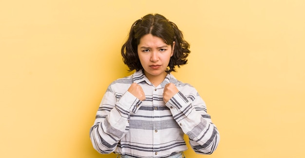 Pretty hispanic woman looking confident angry strong and aggressive with fists ready to fight in boxing position