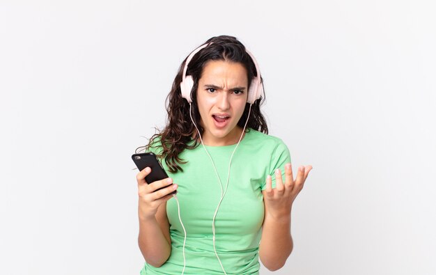 Pretty hispanic woman looking desperate, frustrated and stressed with headphones and a smartphone