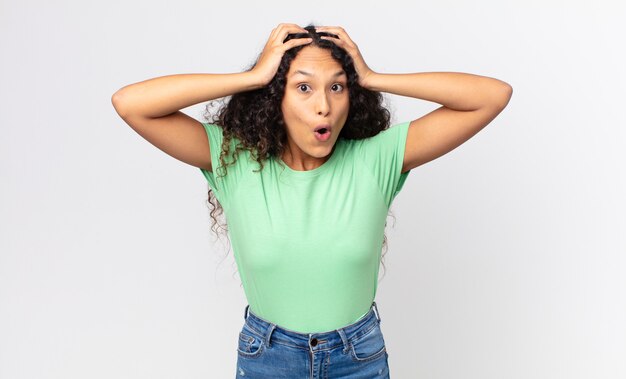 Pretty hispanic woman looking excited and surprised, open-mouthed with both hands on head, feeling like a lucky winner