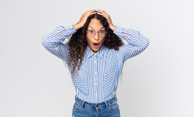 Pretty hispanic woman looking excited and surprised, open-mouthed with both hands on head, feeling like a lucky winner