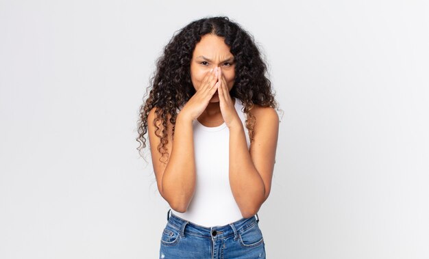 Pretty hispanic woman looking happy, cheerful, lucky and surprised covering mouth with both hands