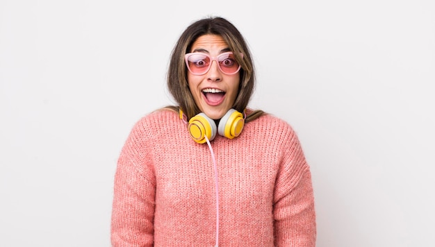 Pretty hispanic woman looking happy and pleasantly surprised headphones concept