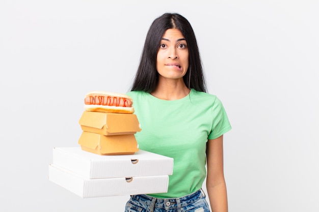 Pretty hispanic woman looking puzzled and confused and holding take away fast food boxes