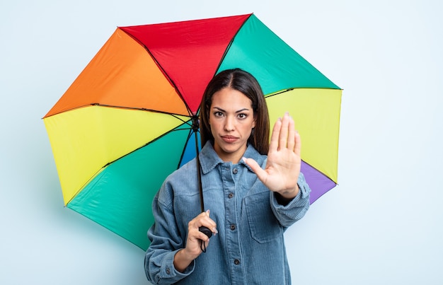 Pretty hispanic woman looking serious showing open palm making stop gesture. umbrella concept