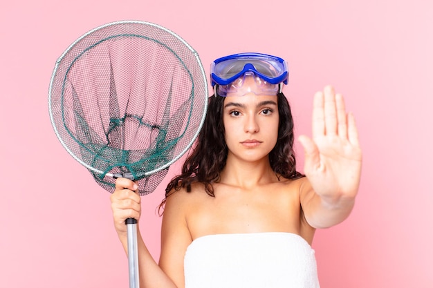 pretty hispanic woman looking serious showing open palm making stop gesture with goggles and fishing net