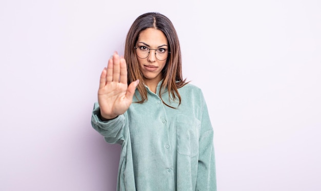 Pretty hispanic woman looking serious, stern, displeased and angry showing open palm making stop gesture