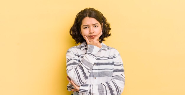 Pretty hispanic woman looking serious thoughtful and distrustful with one arm crossed and hand on chin weighting options