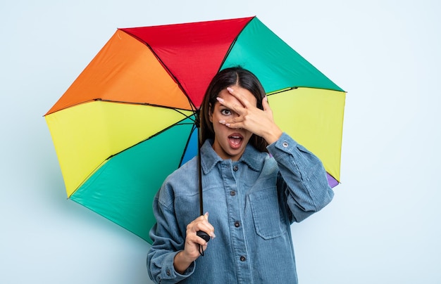 Pretty hispanic woman looking shocked, scared or terrified, covering face with hand. umbrella concept