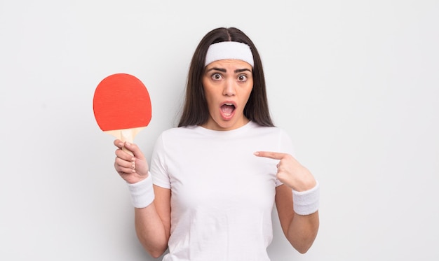 Pretty hispanic woman looking shocked and surprised with mouth wide open pointing to self ping pong concept